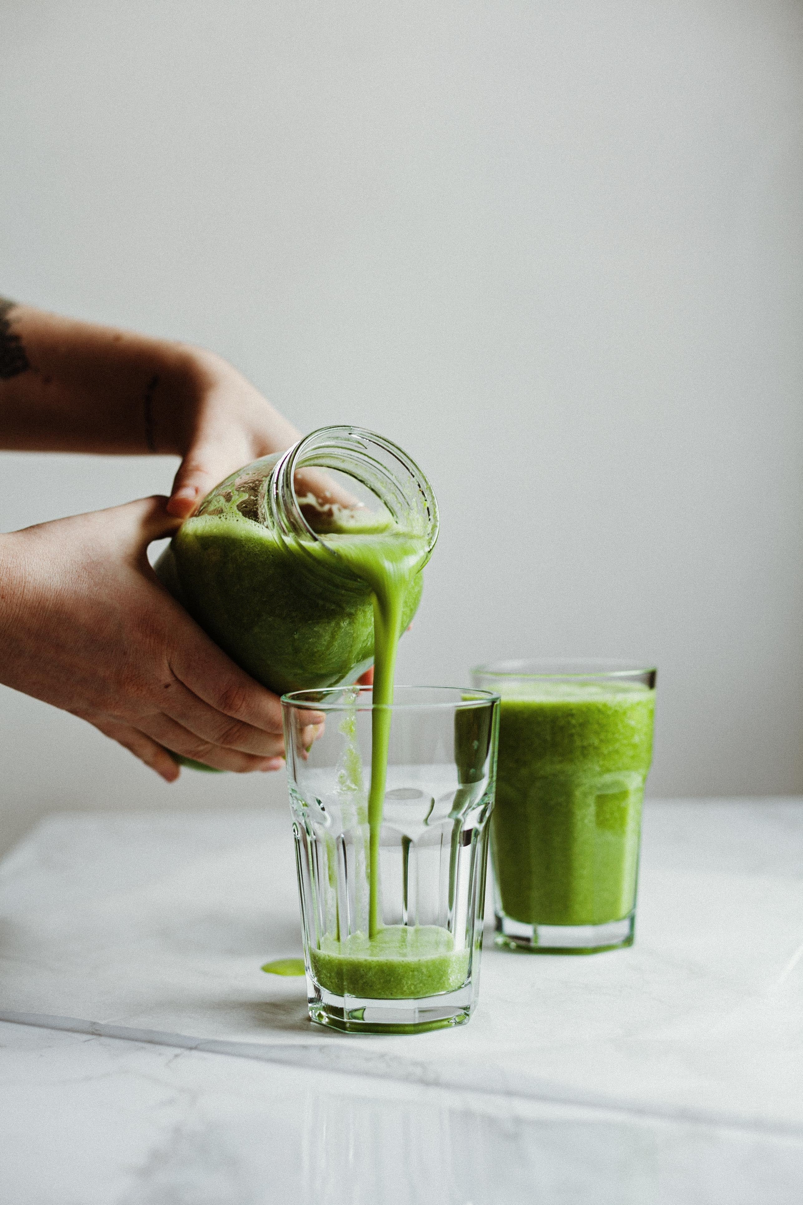 Person serving a green smoothie in a glass