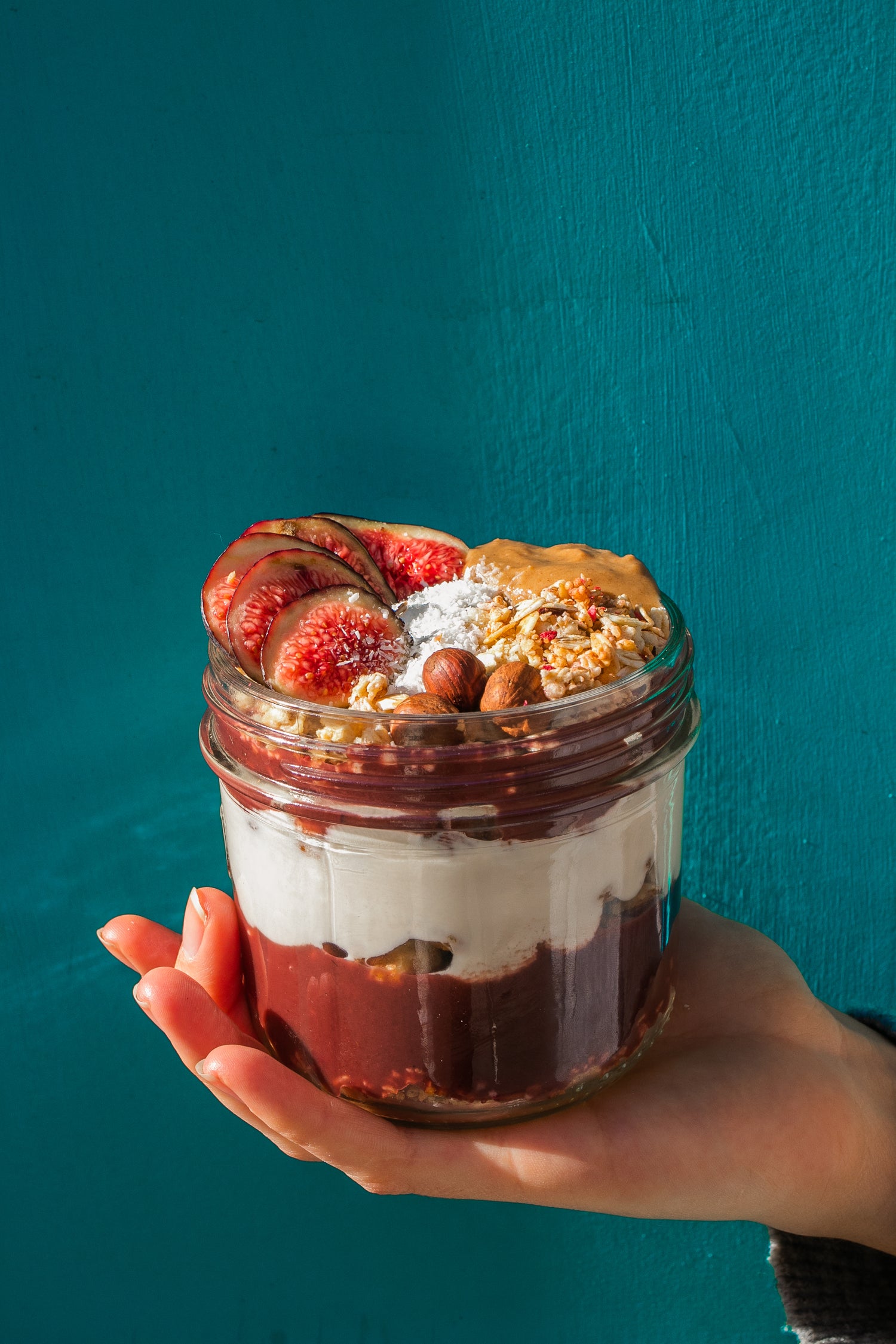 Une main qui tient une verrine à l'acai sur un fond bleu